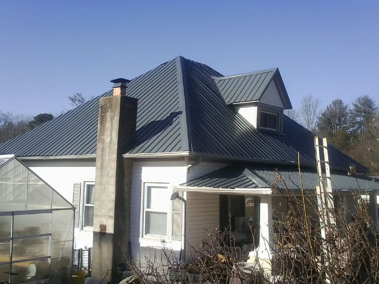 Dark blue standing seam metal roof on a white farmhouse with dormer — Slate & Tile Roof Repair by Roofing Brothers in Merrick