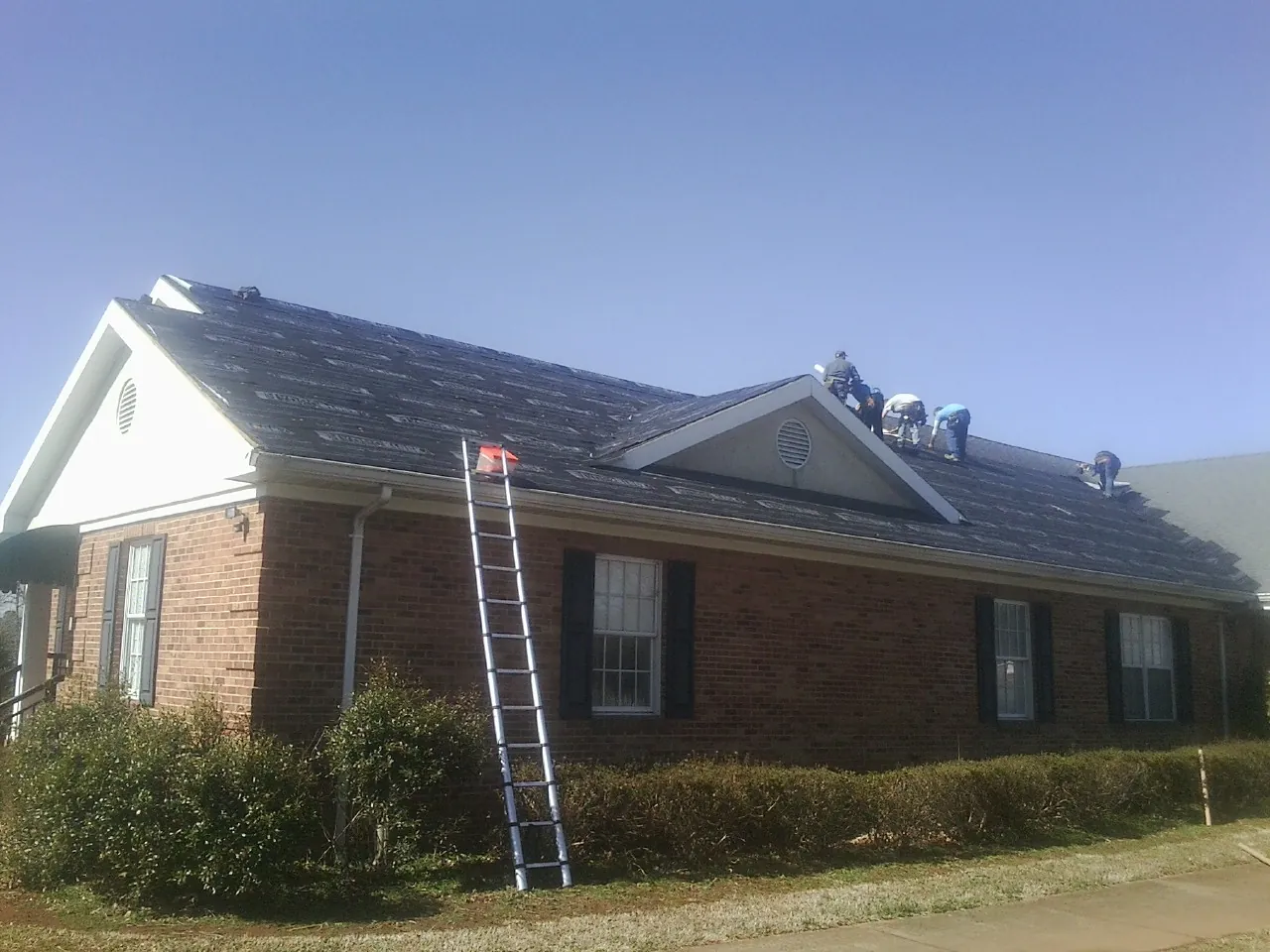 Crew tearing shingles off a brick ranch roof with a ladder set — Emergency Roof Repair work by our crew in Merrick