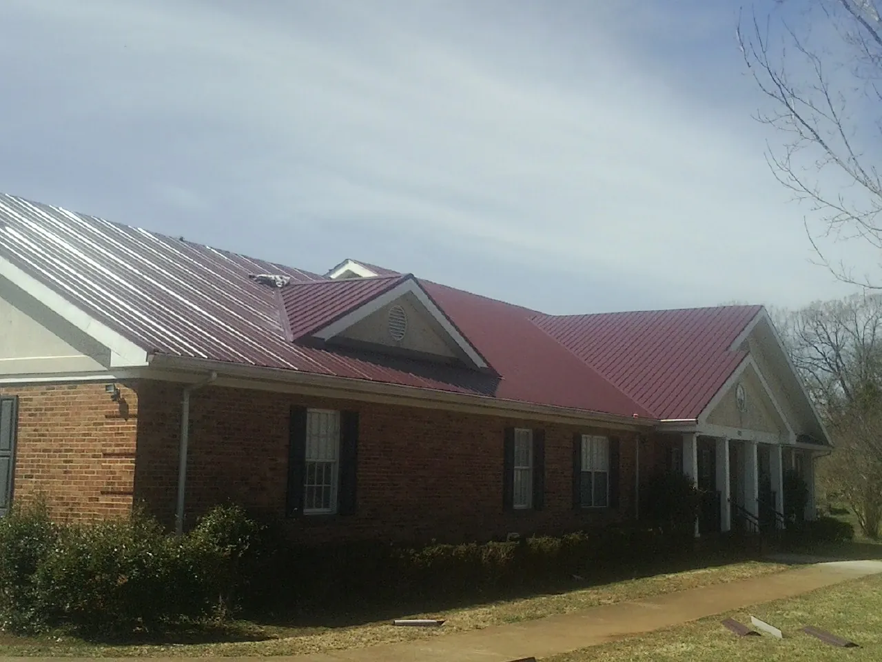Red metal roof with gabled entries on a long brick building, from a Hail Damage Roof Repair job in Merrick