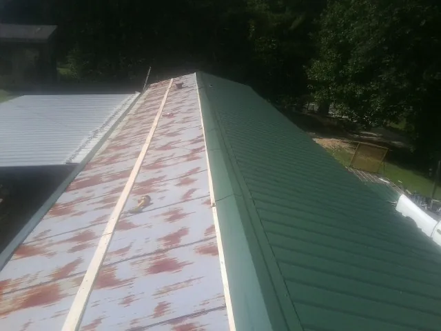 Old rusted panels beside newly installed green metal roofing — Wind Damage Roof Repair by Roofing Brothers in Merrick