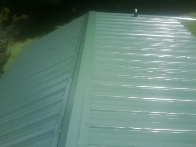 New green metal panels meeting at the ridge of a roof — Flat Roof Repair work by our crew in Merrick