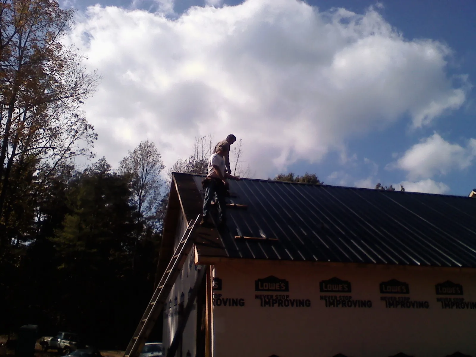 Roofer fastening dark metal panels high against a cloudy sky, from a Roof Inspection job in Merrick