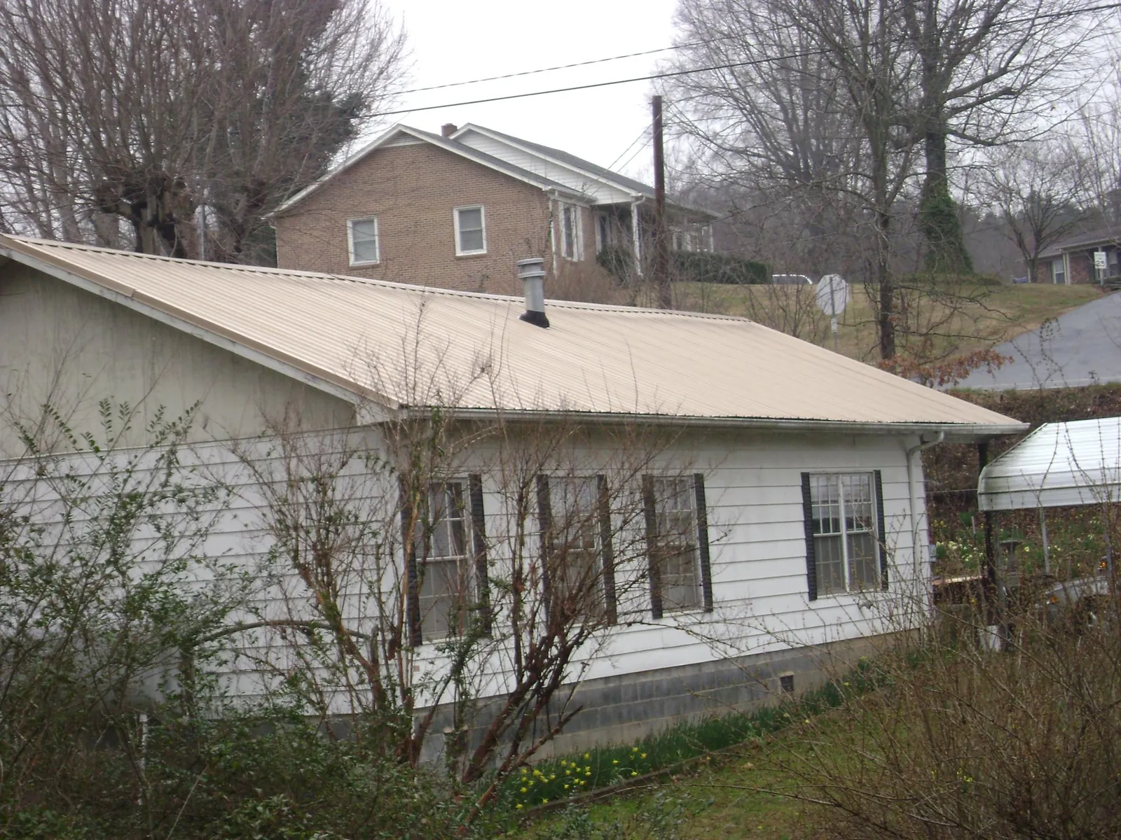 Tan metal roof on a white sided house set into a hillside — Commercial Roofing by Roofing Brothers in Merrick