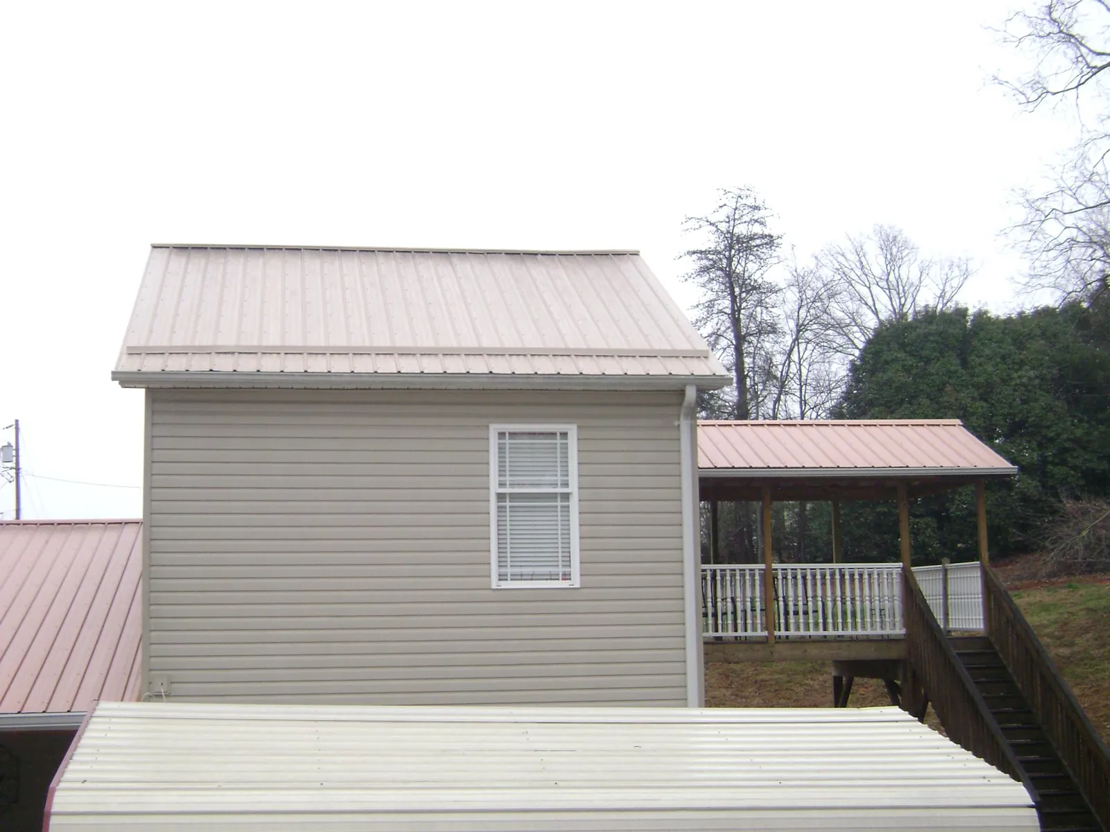 Tan metal roofs on a two story addition and attached porch, from a Roof Replacement job in Merrick
